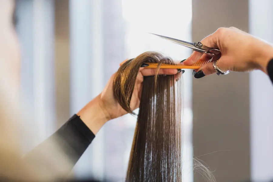Stylist trimming long straight hair with scissors