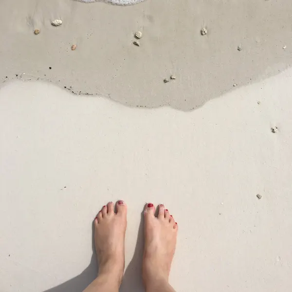 Pedicured feet on a sandy beach at the water’s edge