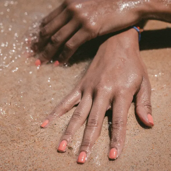 Manicured hands with soft pink polish resting on sand